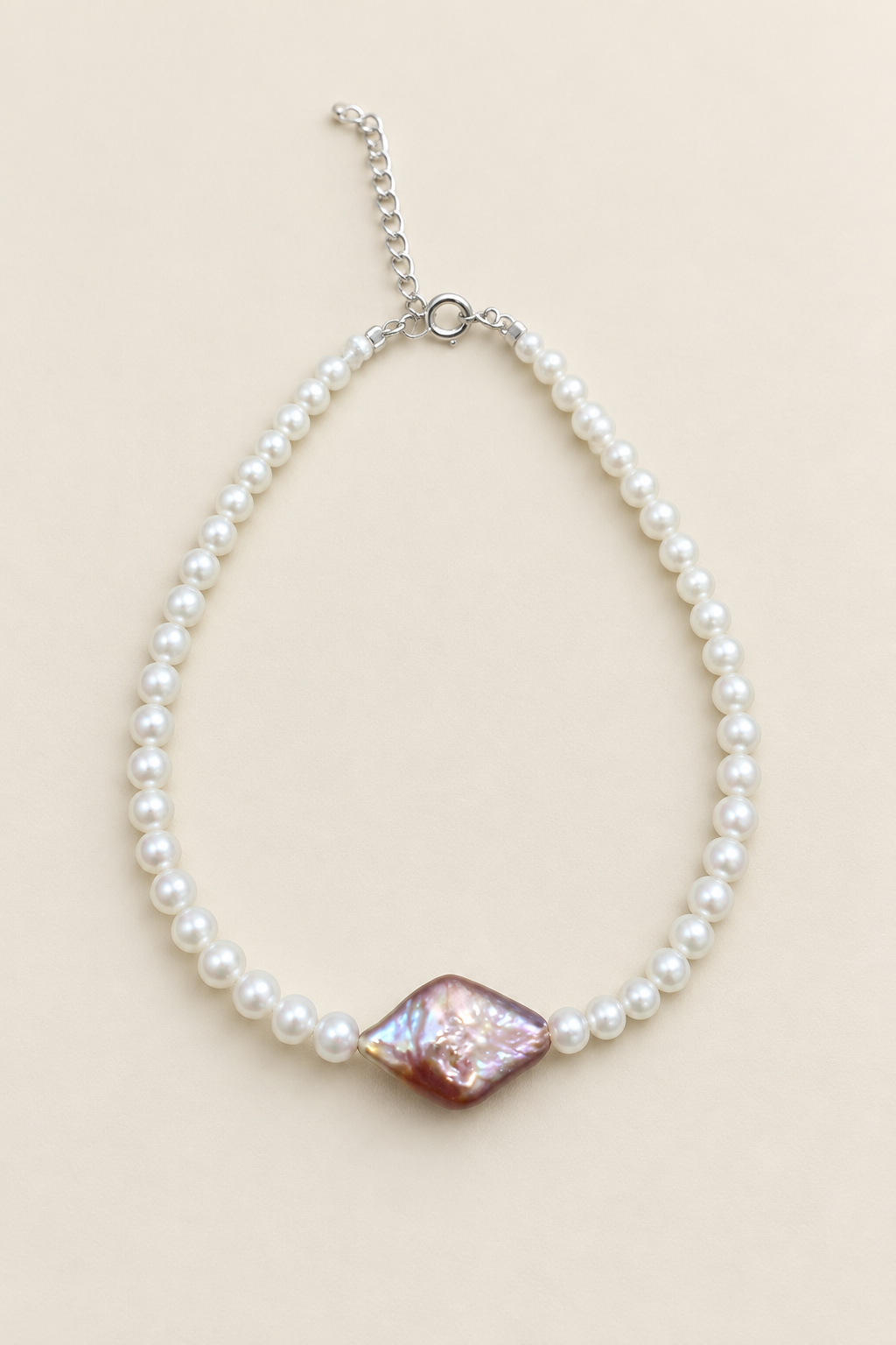 Brilliant white pearl bracelet with purple-pink centre pearl on warm ivory background