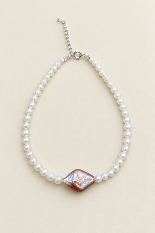 Brilliant white pearl bracelet with purple-pink centre pearl on warm ivory background