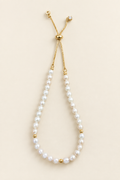 Brilliant white pearl bracelet with gold-tone adjustable chain on warm ivory background